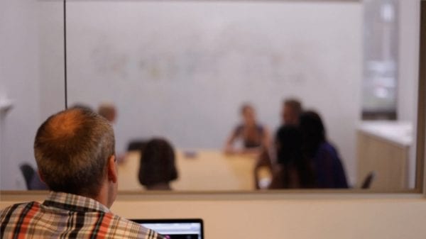 A man observing a workshop session through the observation window