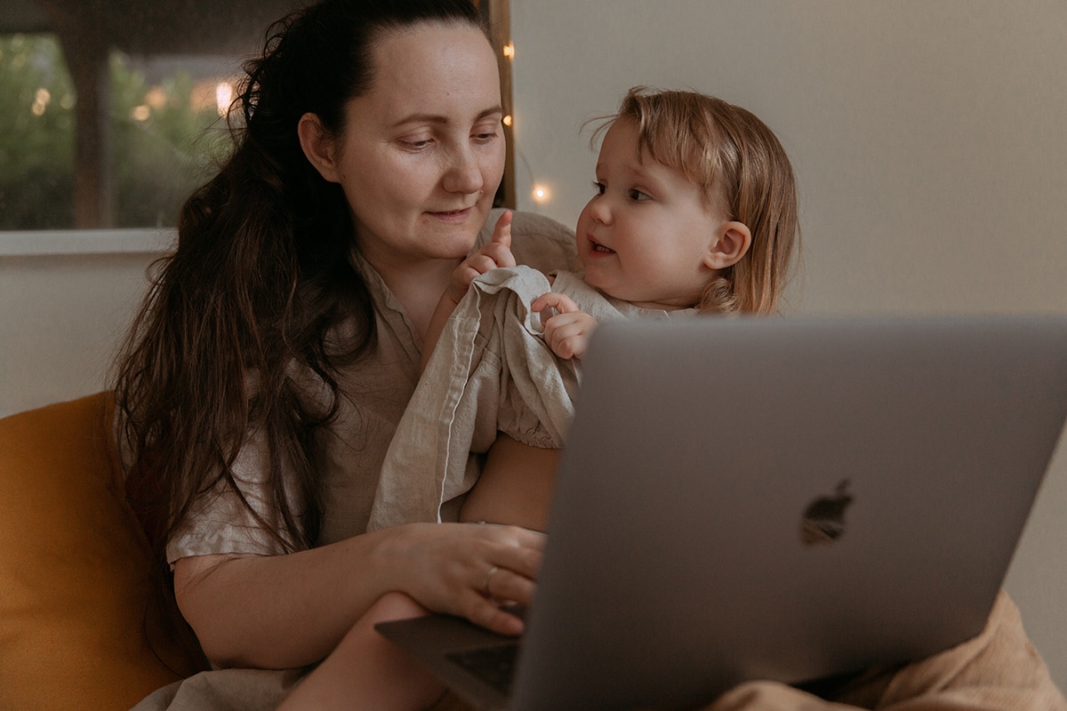 Woman working on laptop with child in her arms